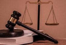 Uma mesa de tribunal com um malhete sobre um livro e a Balança da Justiça ao fundo