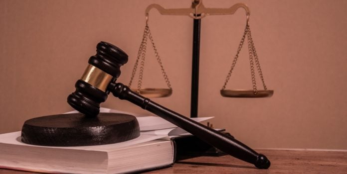 Numero-de-processos-contra-operadores-de-apostas-cresce-mais-de-600-em-2025 Uma mesa de tribunal com um malhete sobre um livro e a Balança da Justiça ao fundo