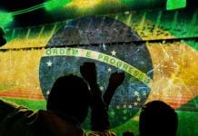 Torcedores celebrando com a badeira do Brasil no fundo da imagem