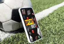 Um celular exibindo apostas esportivas apoiado em uma bola de futebol no gramado de um campo
