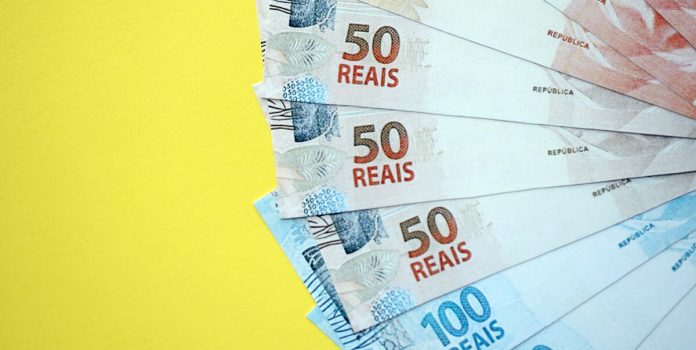 Notas de 50 e 100 reais sobre um fundo amarelo