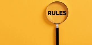 Uma lupa em um fundo amarelo, destacando a palavra "regras" em inglês