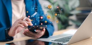 Grupo EGB lança playbook sobre publicidade responsável para influenciadores e afiliados Pessoa mexendo em um celular com ícones de redes sociais sendo projetados do dispositivo
