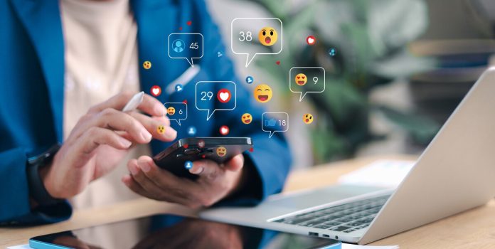 grupo-egb-lança-playbook-sobre-publicidade-responsáve-para-influenciadores-e-afiliados Pessoa mexendo em um celular com ícones de redes sociais sendo projetados do dispositivo