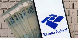 Notas de 100 reais ao lado de celular mostrando o aplicativo da Receita Federal.