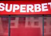 Superbet anuncia linha de acolhimento a apostadores e campanha de R$ 60 milhões para divulgar serviço Letreiro vermelho da Superbet na vitrine, com reflexos.