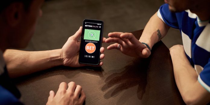 ABC-BET-Pede-Fortalecimento-da-Regulacao-Em-Meio-A-Debate-Sobre-Novas-Restricoes-As-Apostas Dois jovens fazendo apostas esportivas em um celular.