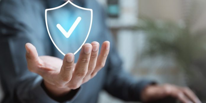 BETesporte-Adota-Tecnologia-da-Betshield-Para-Reforcar-Monitoramento-de-Jogo-Responsavel Um homem estende a mão em direção a uma tela que exibe um escudo azul. O escudo apresenta um símbolo de verificação.