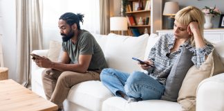 Campinas inclui teleatendimento para atender demandas de ludopatia Um casal sentado no sofá, mexendo no celular, representando a ludopatia