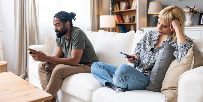 Um casal sentado no sofá, mexendo no celular, representando a ludopatia