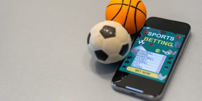 Rodrigo-Capelo-Avalia-Que-Fim-das-Casas-de-Apostas-Ampliaria-Calotes-de-Clubes Bola de futebol e de basquete ao lado de um celular com um aplicativo de apostas esportivas.