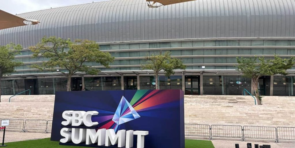 Foto tirada da placa do SBC Summit 2026 em frente à MEO Arena em Lisboa.
