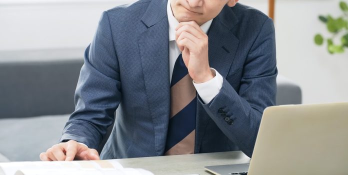 Executivo sentado em frente ao computador com cara de pensativo e preocupado
