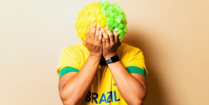 Homem triste vestindo a camiseta do Brasil com as mãos no rosto